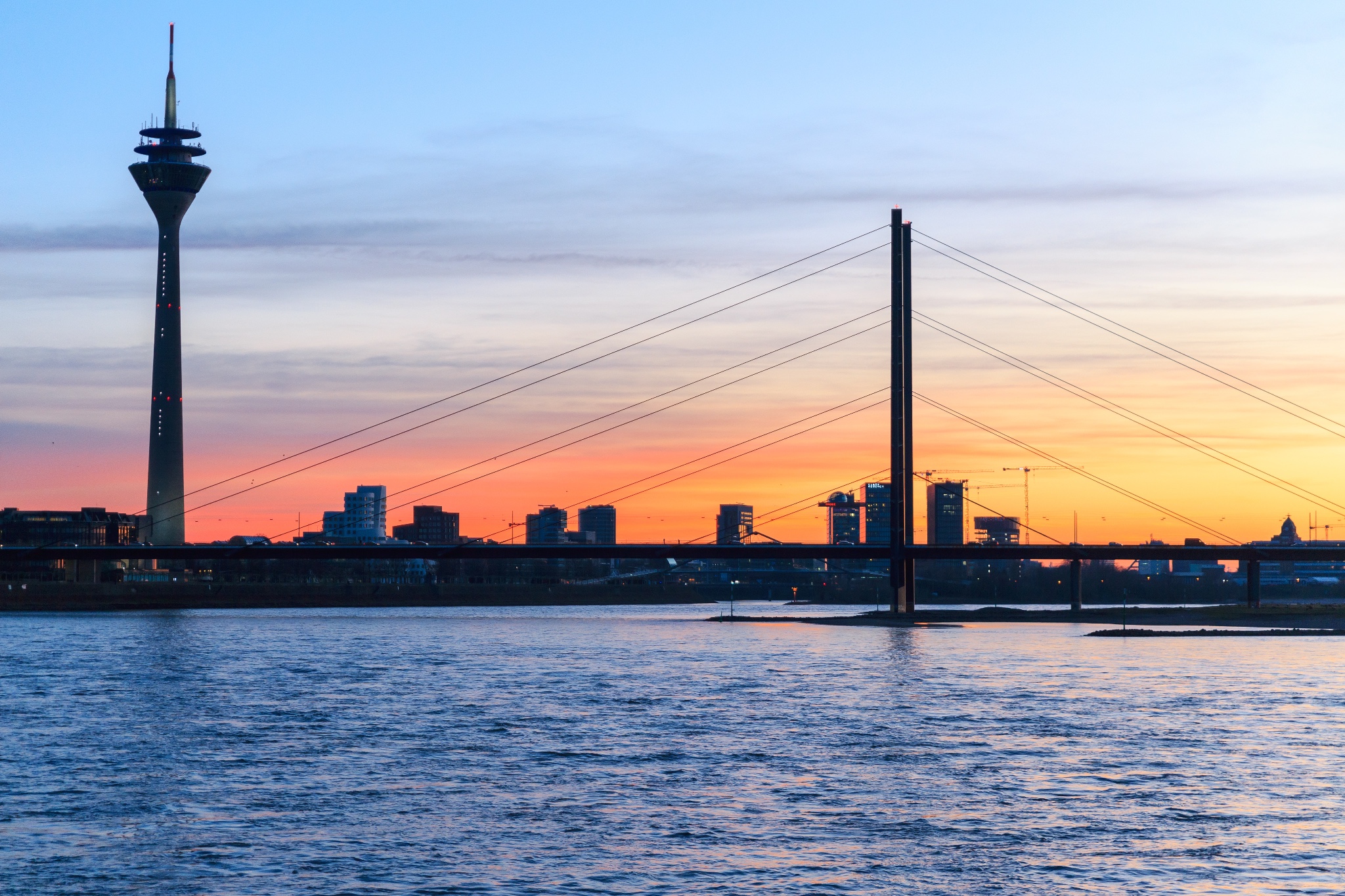 sunset over the riverside of düsseldorf including the rhine, rheinturm and a bridge